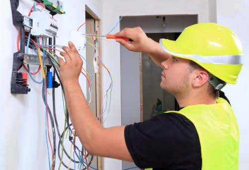 Electrician in a hard hat working on exposed wall wiring