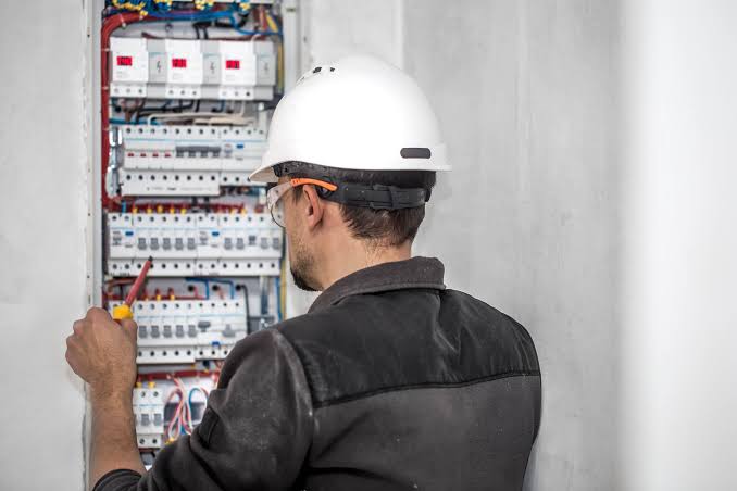 Electrician in a hard hat working on a breaker panel
